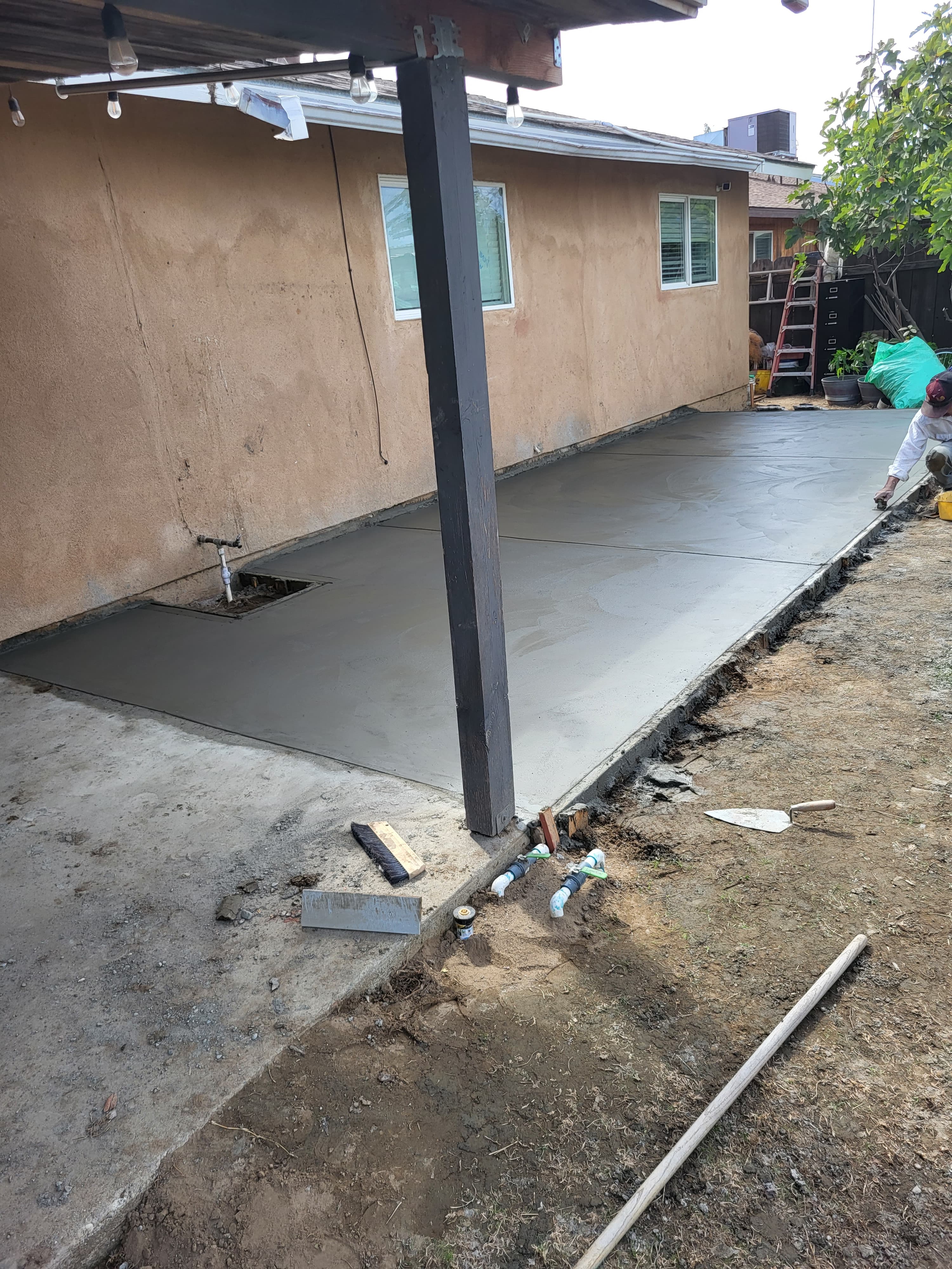 A worker levels freshly poured concrete for a new walkway next to a tan house.
