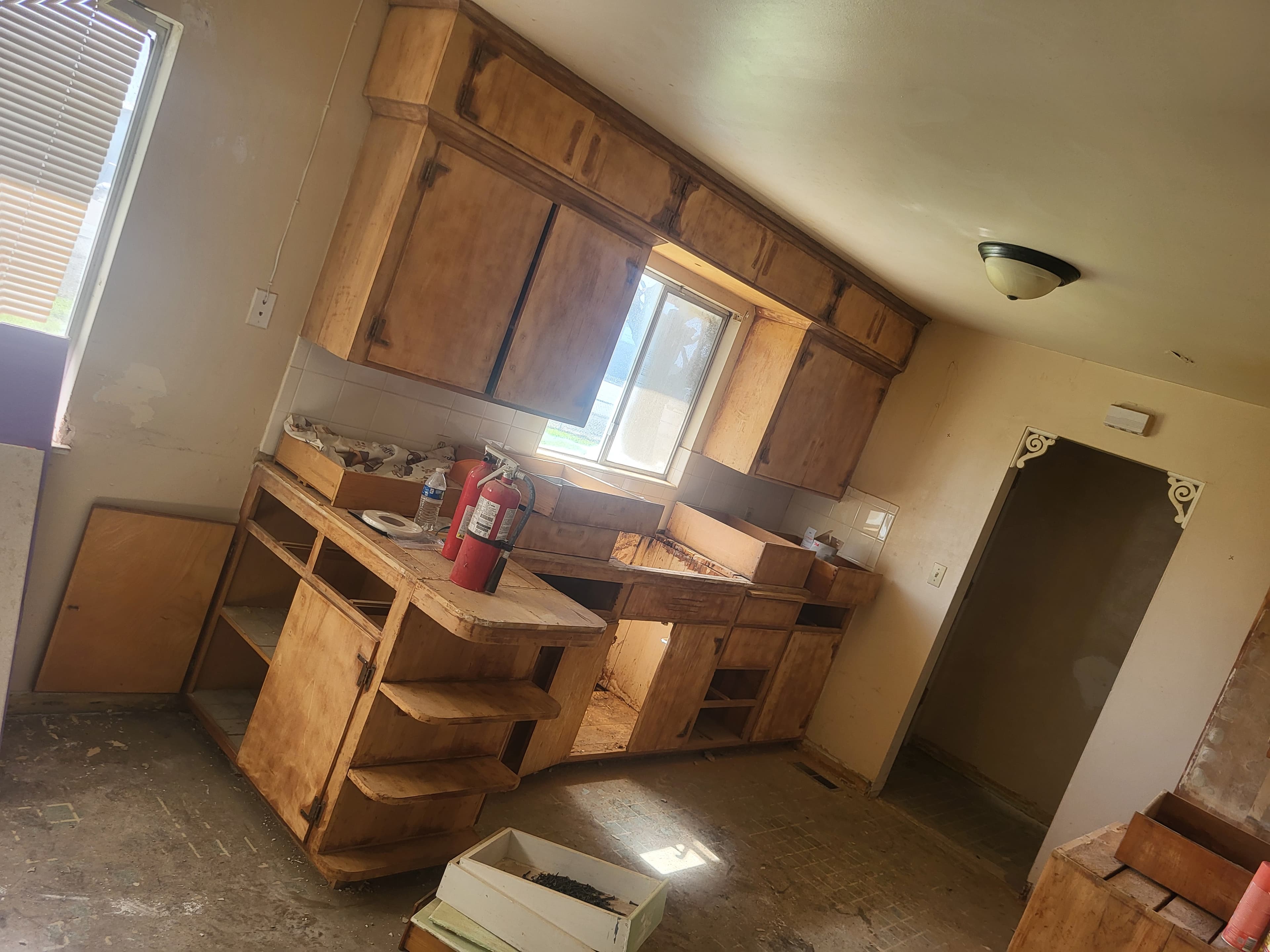 Old wooden kitchen cabinets in a state of disrepair with two red fire extinguishers.