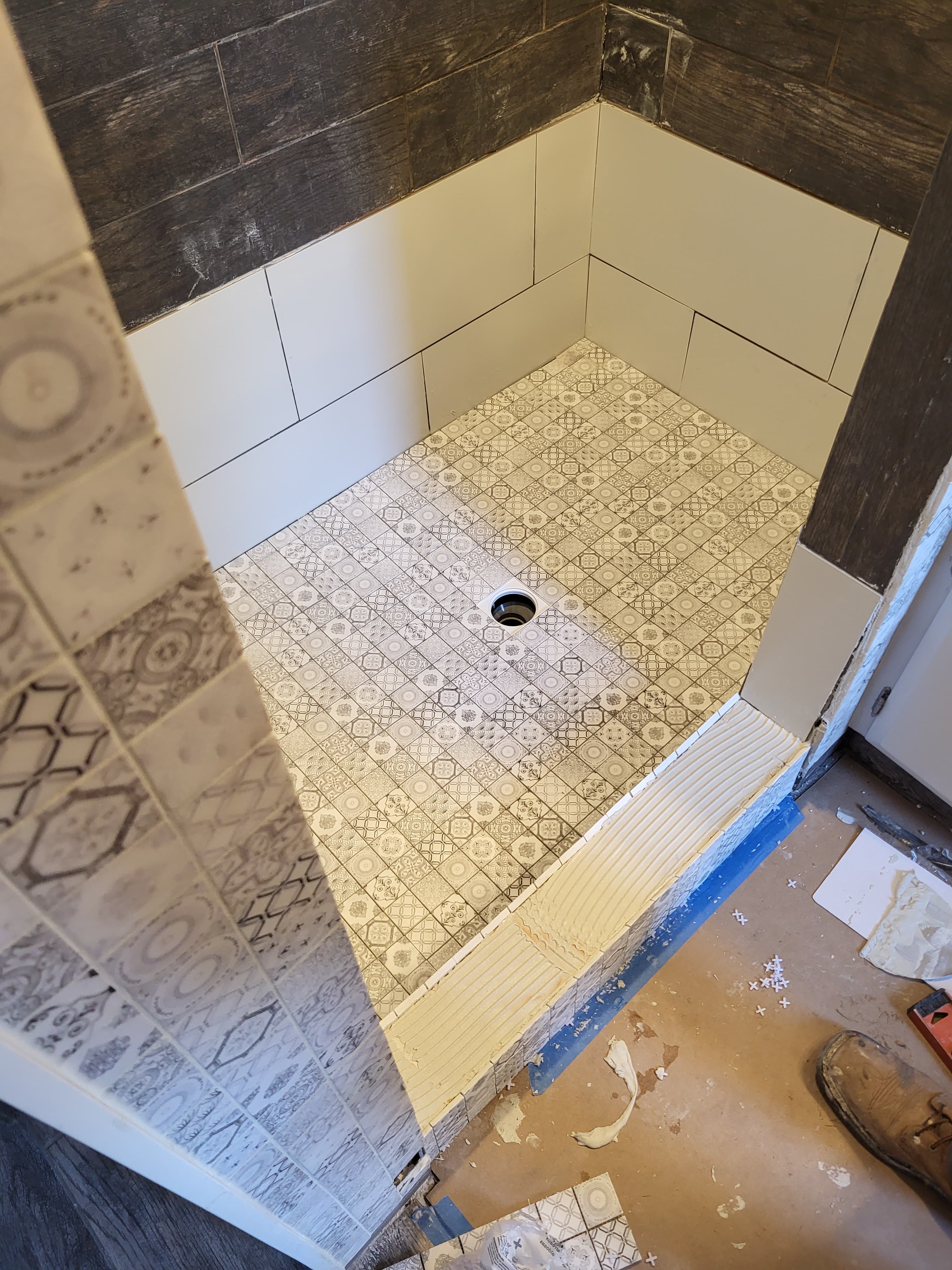 Patterned grey and white mosaic shower floor with central drain during a bathroom tiling project.