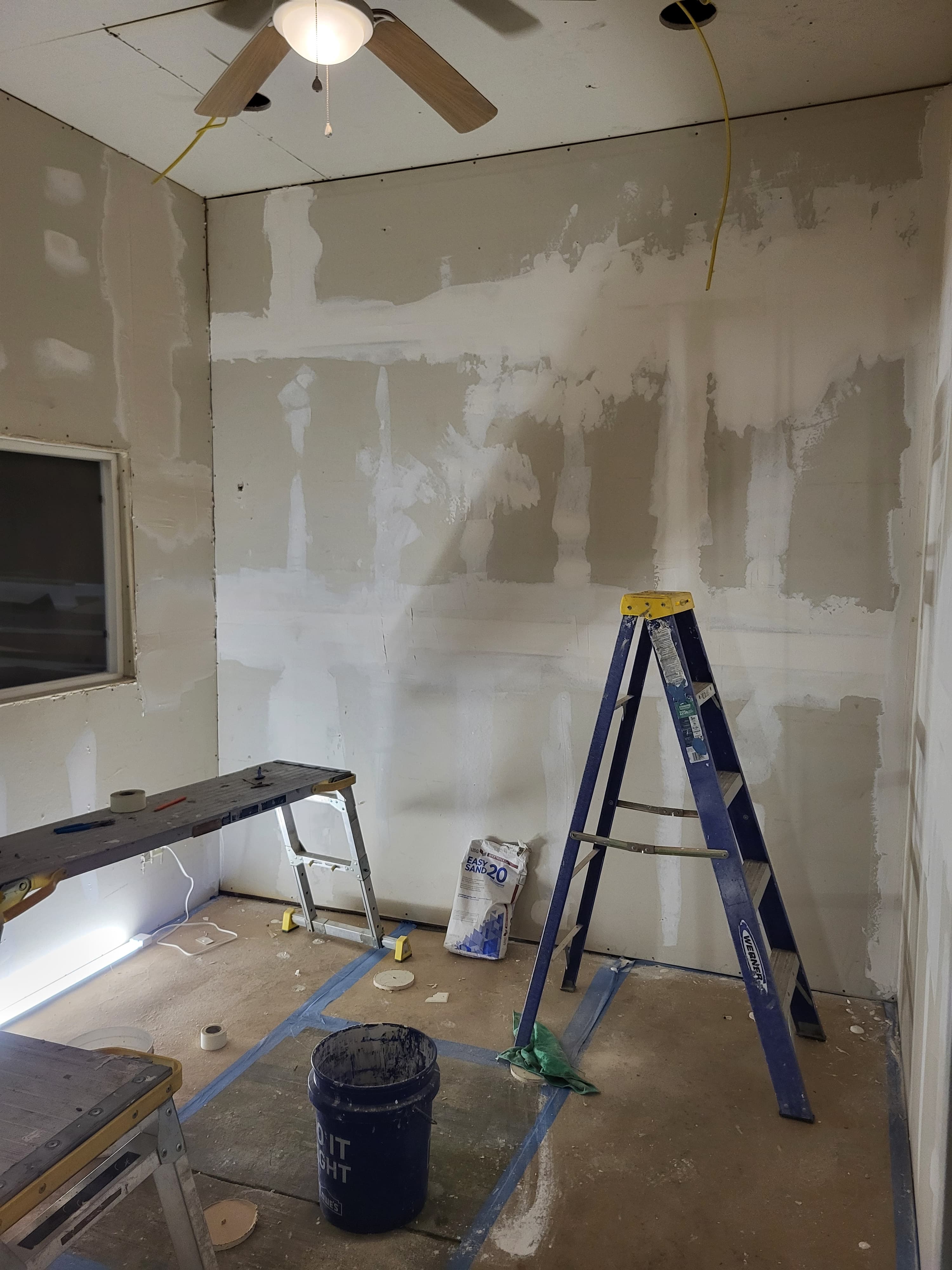 Drywall renovation in a room with joint compound, a blue ladder, and construction supplies.