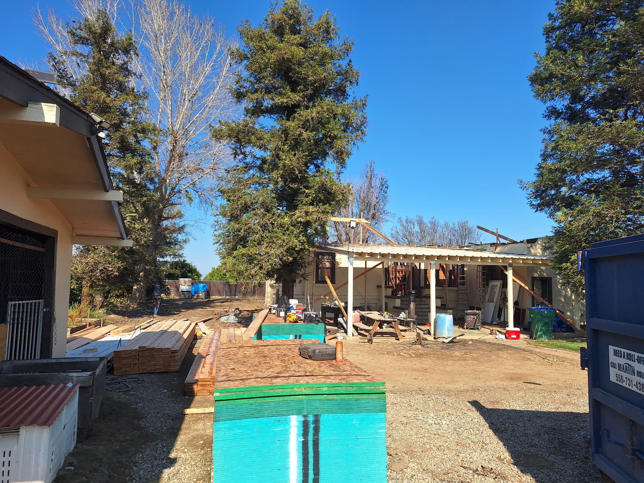 Residential construction site with stacks of lumber and plywood under a clear blue sky.