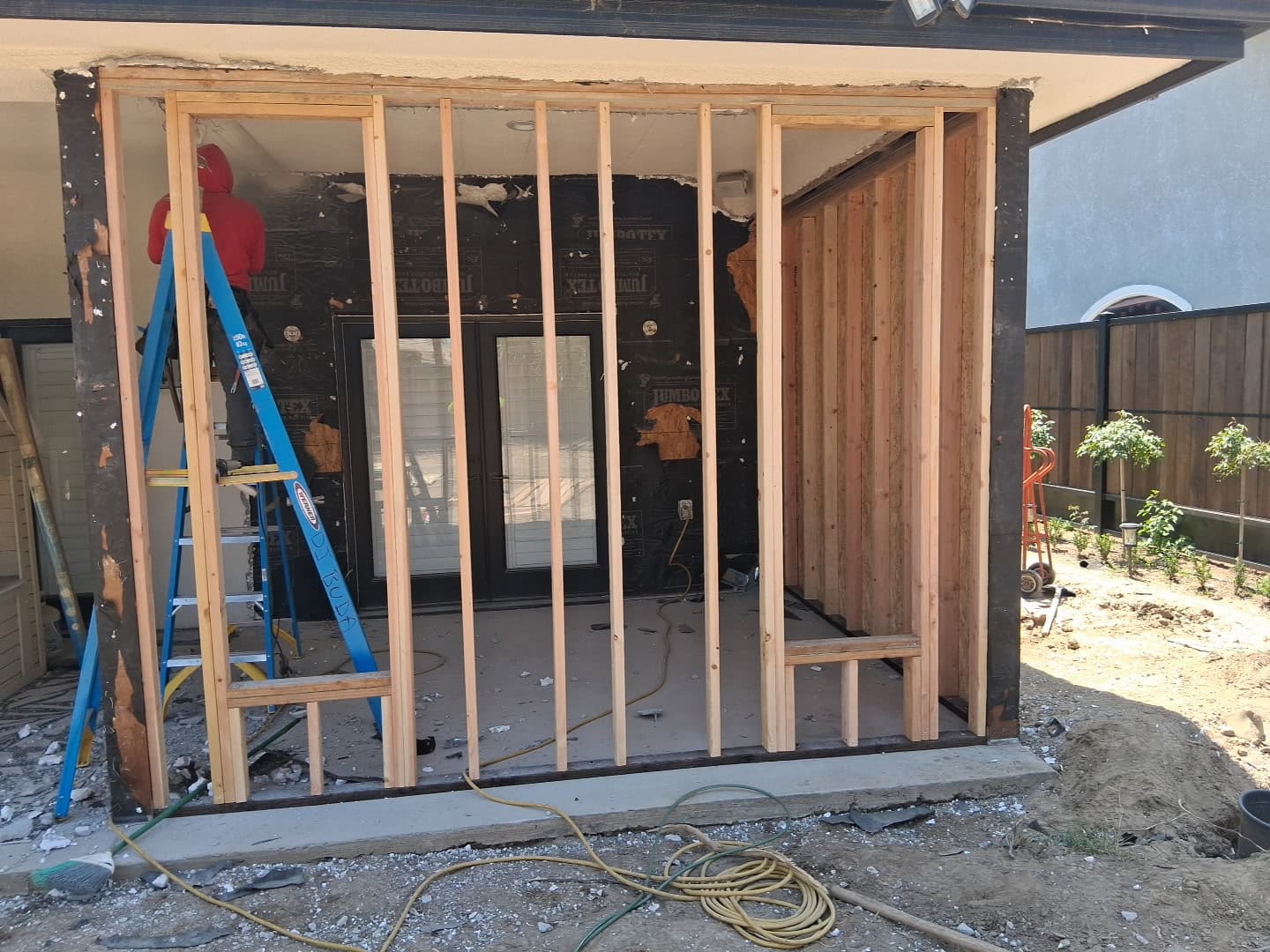 Worker on a blue ladder installs wooden wall studs for a home renovation project.