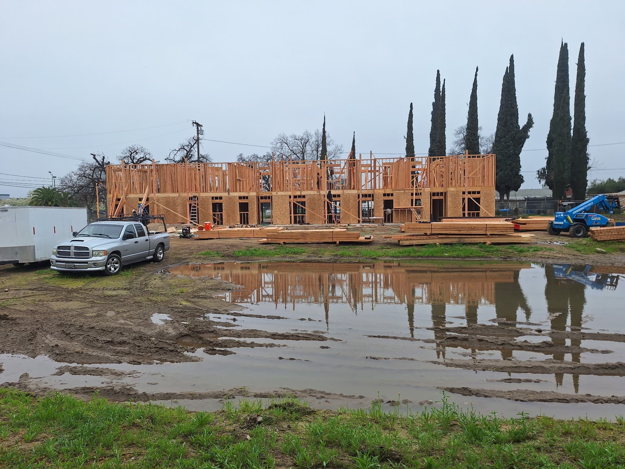 Wooden building frame under construction reflected in large puddles on a muddy site.